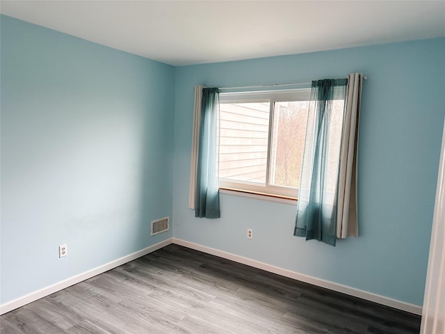 spare room with baseboards, visible vents, and wood finished floors