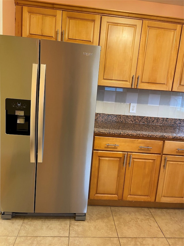 kitchen with stainless steel fridge, brown cabinets, light tile patterned flooring, and dark stone counters
