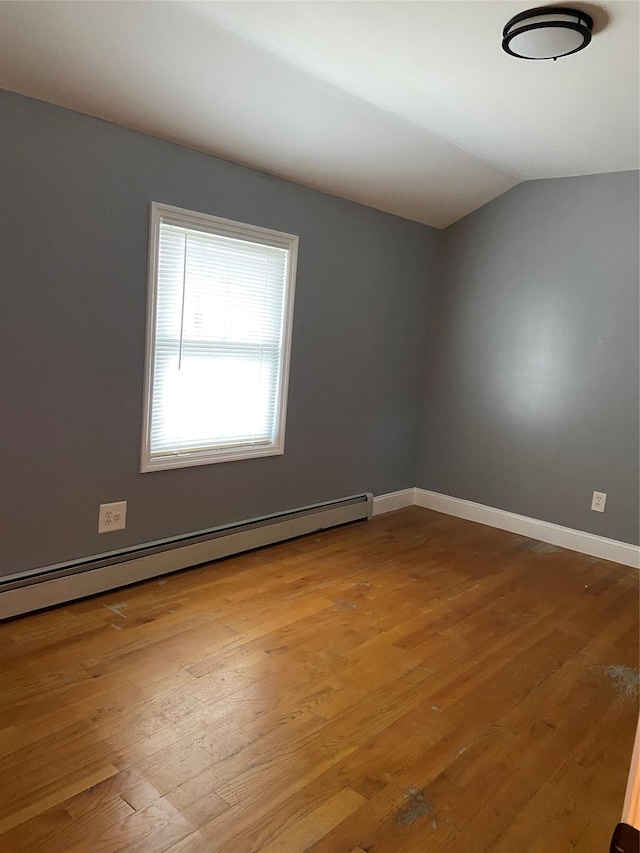 empty room featuring hardwood / wood-style floors, baseboard heating, vaulted ceiling, and baseboards
