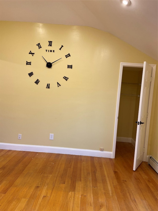 empty room featuring baseboard heating, light wood finished floors, vaulted ceiling, and baseboards