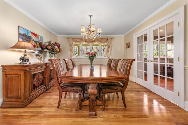 dining space featuring an inviting chandelier, french doors, crown molding, and light wood-style flooring