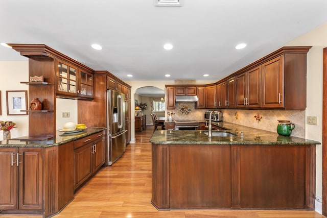 kitchen featuring open shelves, stainless steel appliances, under cabinet range hood, arched walkways, and a peninsula
