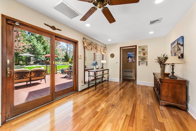 doorway to outside featuring visible vents, light wood-type flooring, a ceiling fan, and radiator