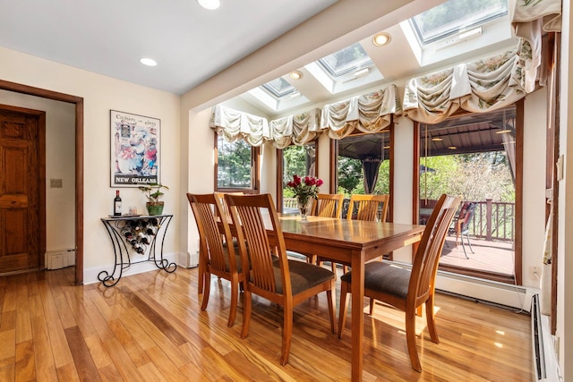 dining room featuring a baseboard radiator, baseboards, recessed lighting, light wood finished floors, and a skylight