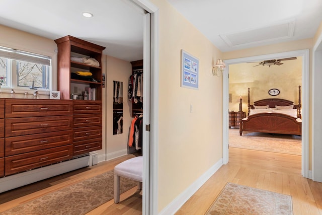 corridor featuring attic access, light wood finished floors, a baseboard heating unit, and baseboards