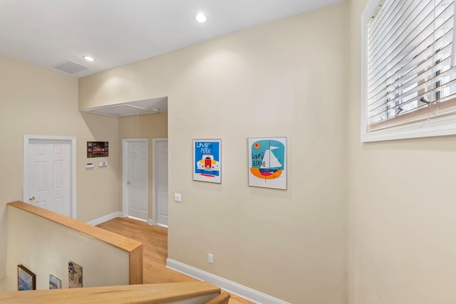 hall with wood finished floors, attic access, an upstairs landing, baseboards, and visible vents
