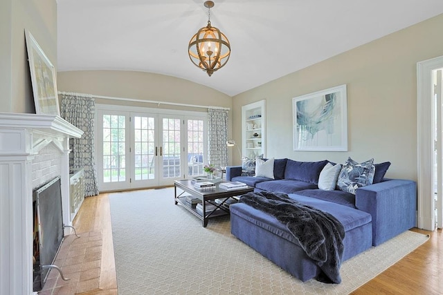 living area with an inviting chandelier, a brick fireplace, light wood-style floors, built in shelves, and french doors