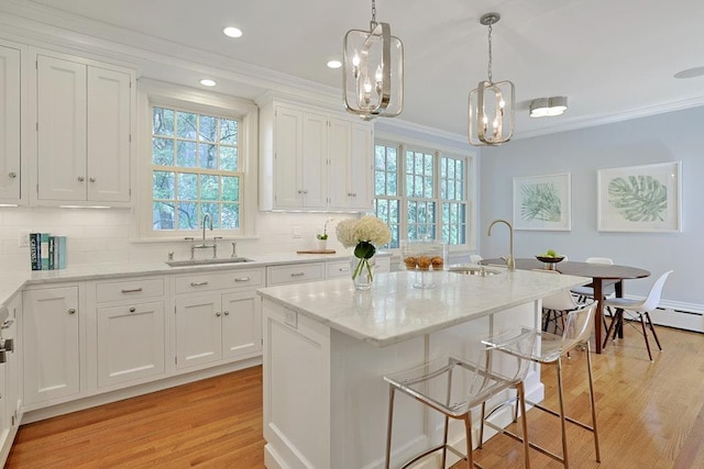 kitchen featuring crown molding, a sink, light wood finished floors, and white cabinetry