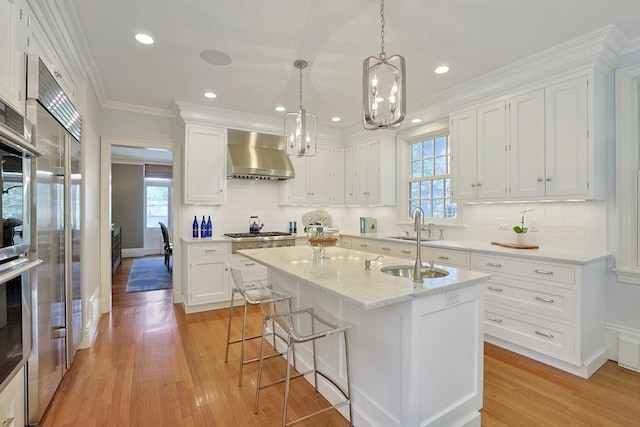 kitchen with wall chimney range hood, white cabinets, stainless steel gas cooktop, and plenty of natural light