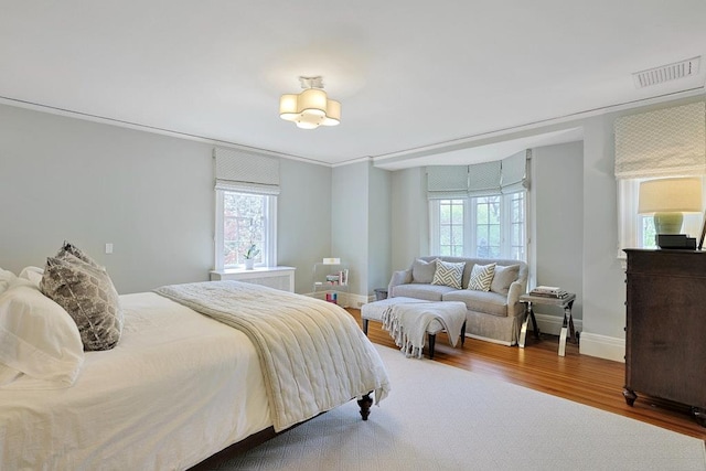 bedroom featuring visible vents, baseboards, wood finished floors, and multiple windows