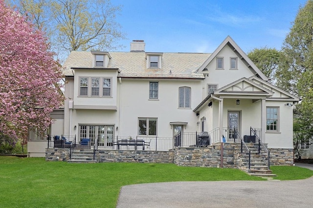 back of house with french doors, stucco siding, a chimney, a patio area, and a lawn