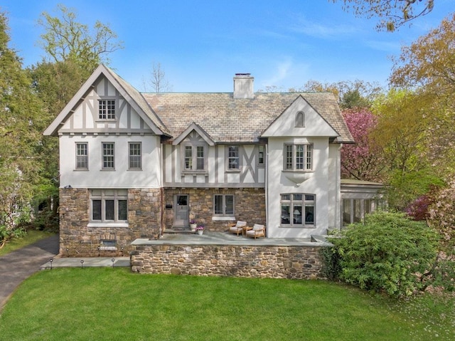 back of house featuring a yard, a chimney, stone siding, and stucco siding