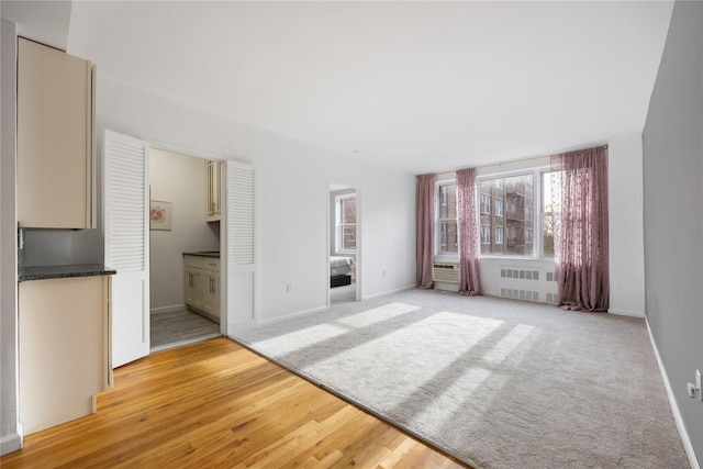 unfurnished living room featuring radiator heating unit, light wood-style floors, and baseboards