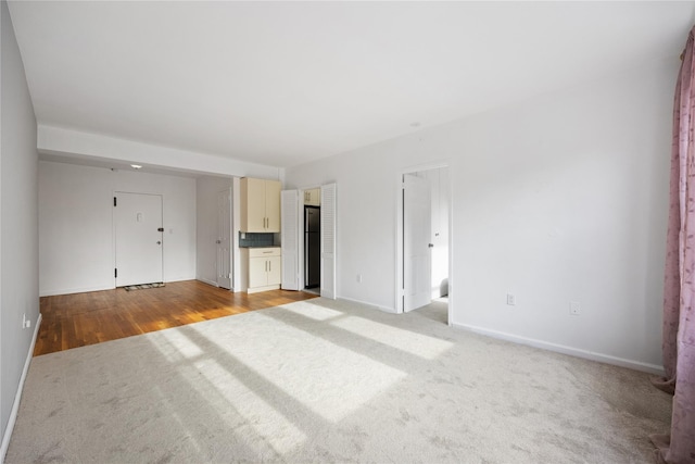 unfurnished bedroom with baseboards, connected bathroom, carpet, and freestanding refrigerator