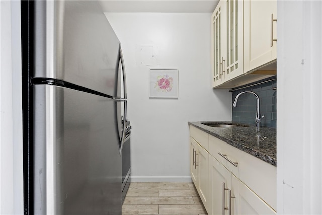 kitchen featuring dark stone countertops, tasteful backsplash, glass insert cabinets, freestanding refrigerator, and a sink