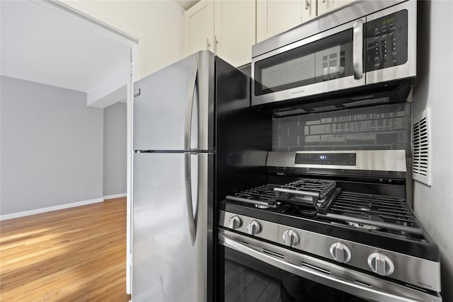 kitchen featuring light wood-style floors, tasteful backsplash, white cabinetry, baseboards, and appliances with stainless steel finishes