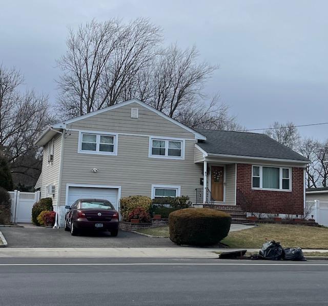 tri-level home with brick siding, a garage, fence, and driveway