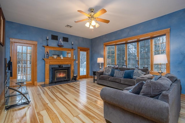 living room featuring light wood-style floors, a high end fireplace, ceiling fan, and visible vents