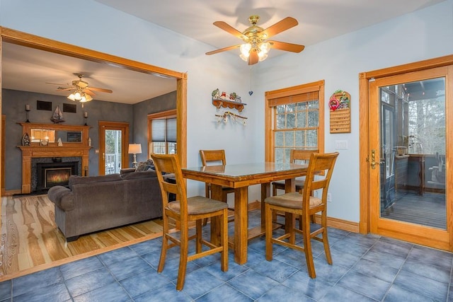tiled dining area featuring baseboards, ceiling fan, and a lit fireplace