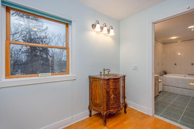 bathroom with baseboards, vanity, tiled tub, and wood finished floors