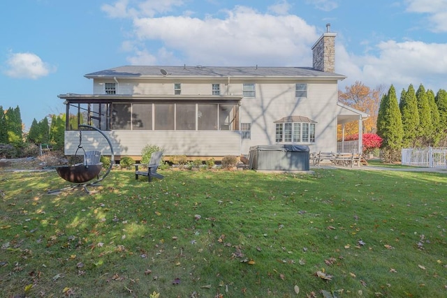back of property featuring a sunroom, a yard, a chimney, and a hot tub