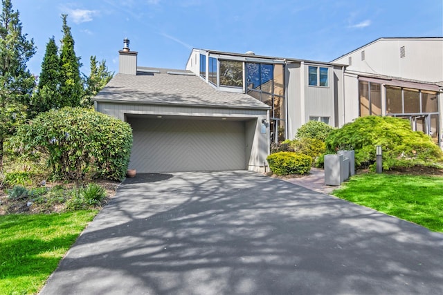view of front of house featuring a garage, a chimney, a shingled roof, and aphalt driveway