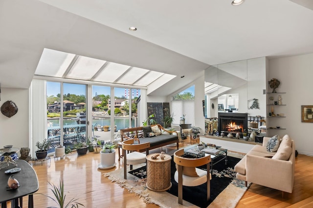 living room featuring wood finished floors, lofted ceiling, a warm lit fireplace, recessed lighting, and a water view