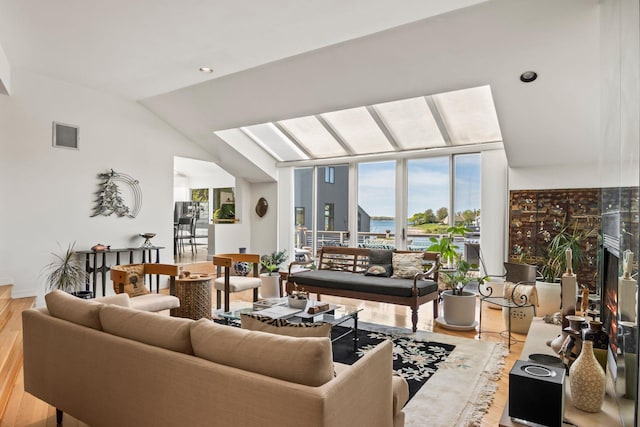 living room featuring a water view, visible vents, wood finished floors, and lofted ceiling with skylight