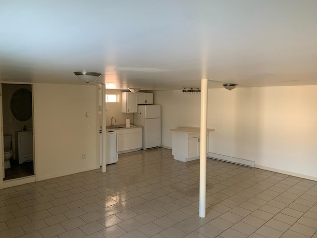 below grade area featuring baseboard heating, freestanding refrigerator, and a sink