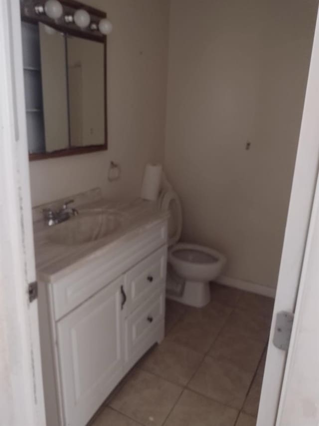 half bathroom featuring toilet, vanity, tile patterned flooring, and baseboards