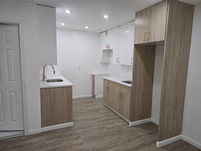 kitchen with a sink, light countertops, light wood-style flooring, recessed lighting, and baseboards