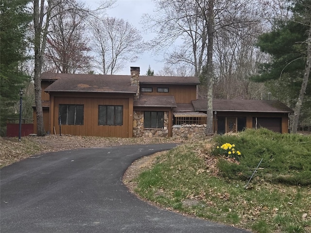 view of front of home with a chimney, stone siding, aphalt driveway, and an attached garage