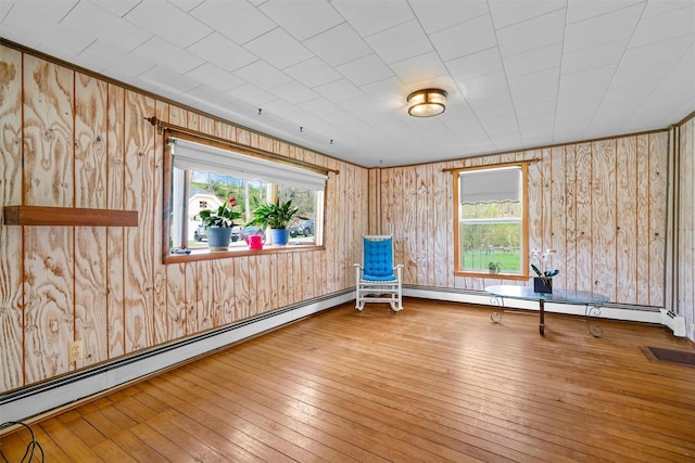 unfurnished room with wooden walls, a baseboard radiator, and hardwood / wood-style floors