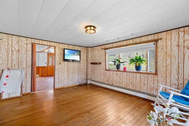 interior space with wood-type flooring, wood walls, and a baseboard heating unit