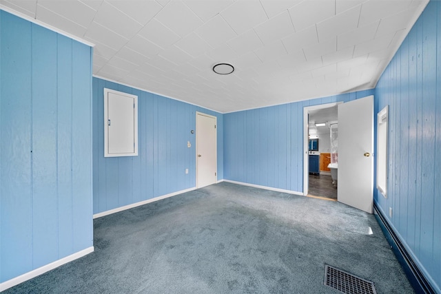 unfurnished bedroom featuring a baseboard heating unit, wood walls, visible vents, and carpet floors