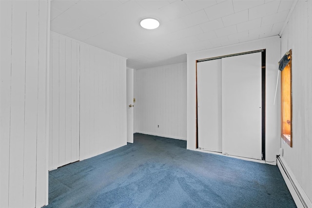 unfurnished bedroom featuring a closet, wood walls, a baseboard radiator, and carpet floors