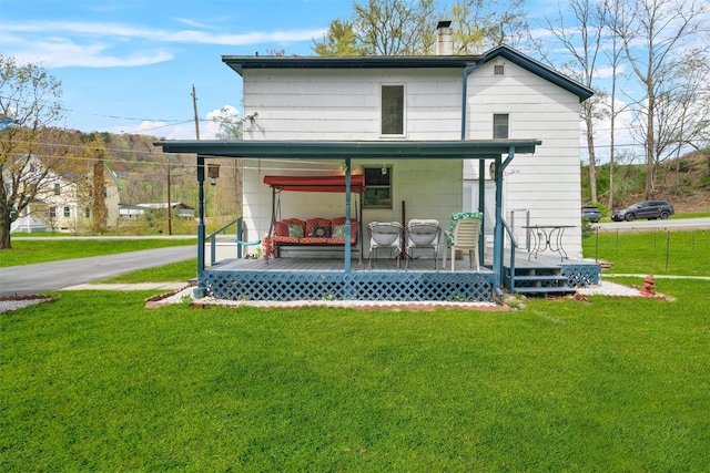 back of property with a yard, a chimney, driveway, covered porch, and a carport