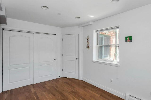unfurnished bedroom featuring a closet, recessed lighting, a baseboard heating unit, dark wood-style flooring, and baseboards