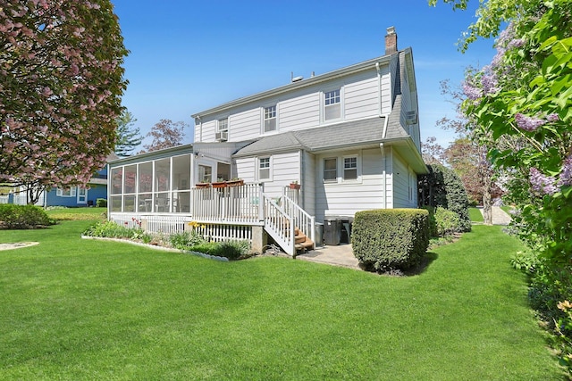 rear view of property with a yard, a chimney, a sunroom, and a wooden deck
