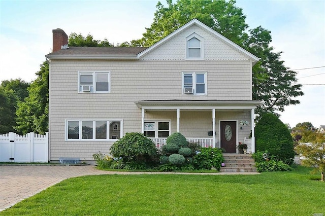 view of front facade with fence, a chimney, a porch, and a front lawn