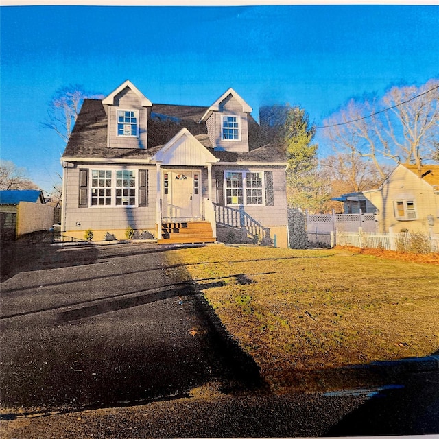 cape cod house featuring fence and a front lawn