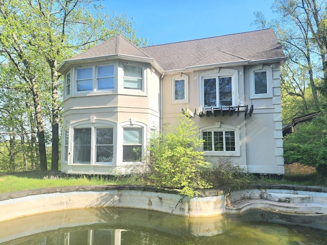 back of property with a shingled roof and stucco siding