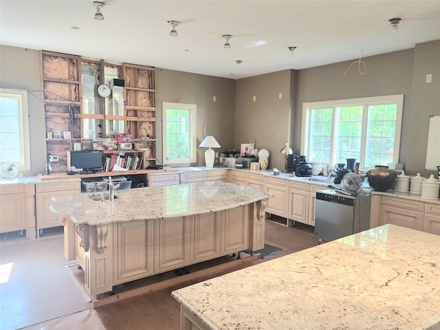kitchen featuring an island with sink, a healthy amount of sunlight, and light stone countertops