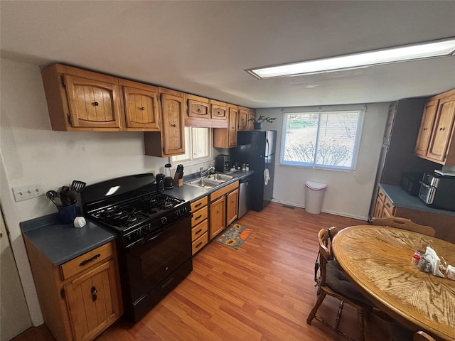 kitchen with a sink, dark countertops, stainless steel appliances, light wood finished floors, and brown cabinetry
