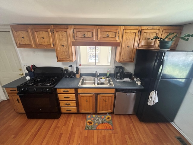 kitchen featuring black appliances, light wood-style flooring, brown cabinetry, and a sink