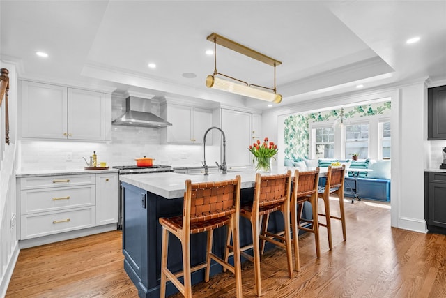 kitchen featuring ornamental molding, a raised ceiling, wall chimney exhaust hood, and decorative backsplash