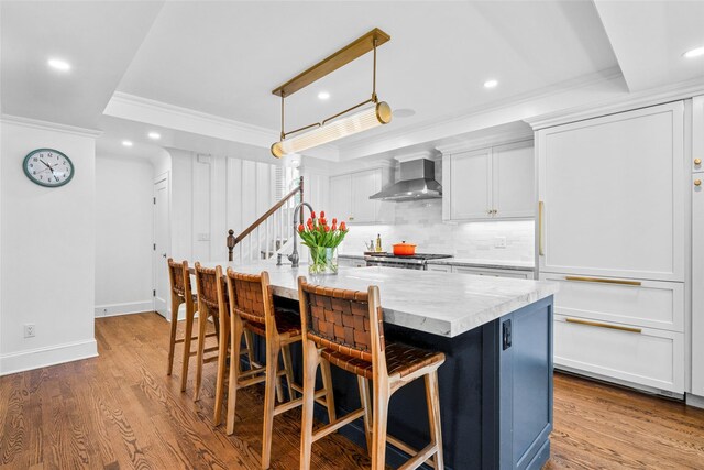 kitchen featuring wall chimney range hood, backsplash, ornamental molding, a tray ceiling, and recessed lighting