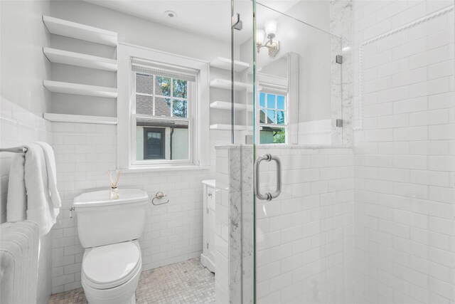 bathroom featuring wainscoting, toilet, tile walls, and a shower stall