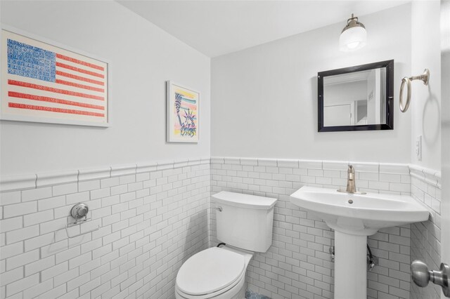 half bathroom with a wainscoted wall, toilet, and tile walls