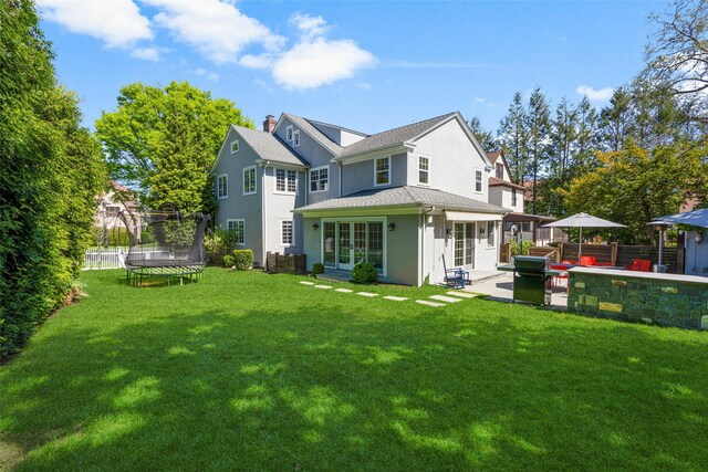 rear view of house featuring a trampoline, a lawn, a patio area, fence, and stucco siding